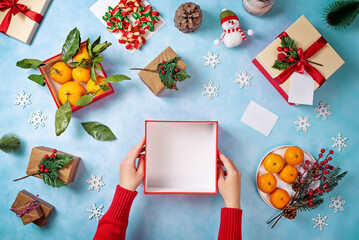 Blue Christmas background with the preparation of gifts by women's hands; boxes; gifts and tangerines