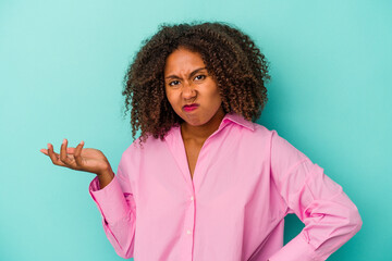 Young african american woman with curly hair isolated on blue background doubting and shrugging...