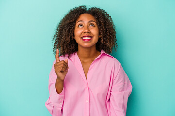 Young african american woman with curly hair isolated on blue background indicates with both fore...