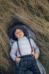 boy child in plaid pants, hat, suspenders and scarf lying on the ground in a field