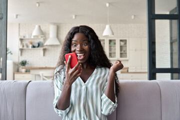 Young African black girl at home reading message on mobile phone on unexpected news, happy client...