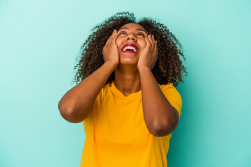 Fototapeta na wymiar Young african american woman with curly hair isolated on blue background laughs joyfully keeping hands on head. Happiness concept.