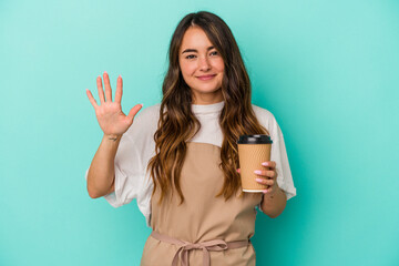 Young caucasian store clerk woman holding a takeaway coffee isolated on blue background smiling cheerful showing number five with fingers.