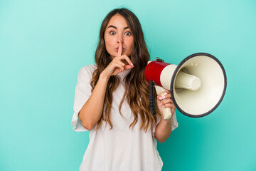 Young caucasian woman holding a megaphone isolated on blue background keeping a secret or asking for silence.