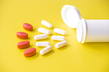 White and red pills are poured from a jar on a yellow background. Food supplement, multivitamins, medications. treatment and prevention of diseases, therapy. wellness