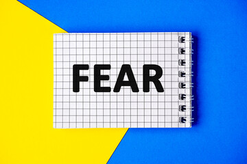 Text FEAR on page notebook with cage lies on a blue and yellow background, top view. First...