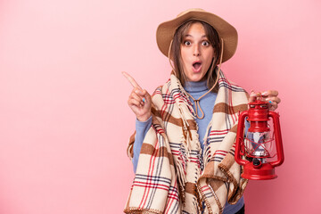 Young caucasian woman holding vintage lantern isolated on pink background pointing to the side