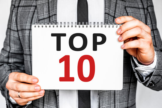 business, technology, internet and networking concept - businessman in gray fashionable business suit holding a white notebook with conference inscription TOP 10 inscription