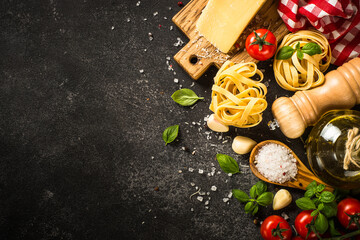Italian food background on black. Raw Pasta, fresh tomatoes, olive oil, spices, parmesan and basil. Top view with copy space.