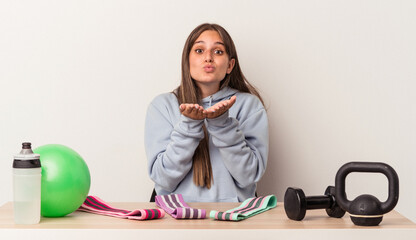 Young caucasian woman sitting at a table with sport equipment isolated on white background folding lips and holding palms to send air kiss.