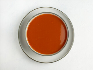 Top view of tomato soup in bowl on plate on white background