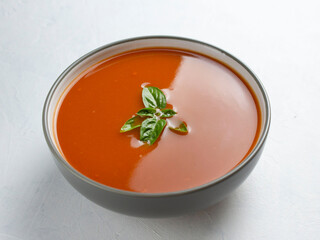 Tomato soup with basil in a gray bowl on a white surface