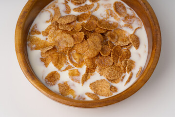 A bowl with corn flakes breakfast and poured milk on a white background.