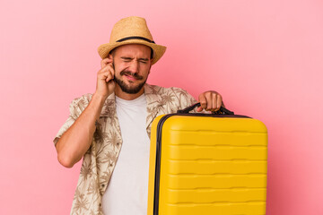 Young caucasian man with tattoos going to travel isolated on pink background  covering ears with...