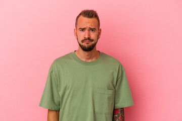 Young caucasian man with tattoos isolated on pink background  sad, serious face, feeling miserable...