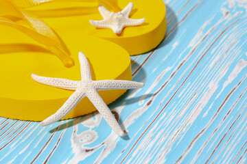 yellow rubber beach flip flops and starfish on a blue wooden background, place under the text