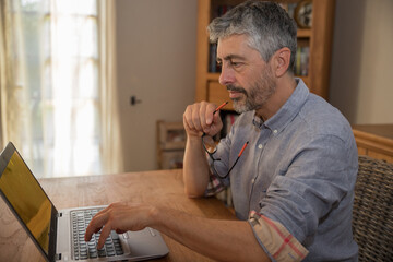 portrait d'un homme de 50 ans en train de travailler à son domicile sur son ordinateur portable