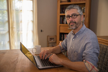 portrait d'un homme de 50 ans en train de travailler à son domicile sur son ordinateur portable