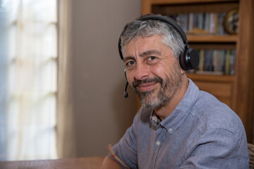 portrait d'un homme de 50 ans souriant au travail avec un micro casque. Il travaille chez lui