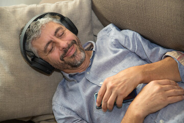 un homme d'âge mûr 50 ans fait la sieste dans son canapé gris en écoutant de la musique avec un...
