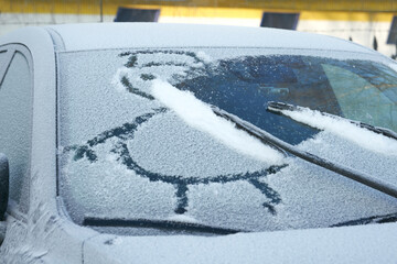 Wiper blades erase a child's drawing of a snowman from the snow-covered front window of the car.