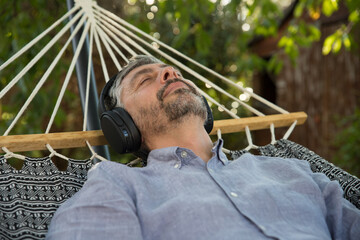 Homme d'âge mur 50 ans se repose dans son hamac en écoutant de la musique avec un casque à l'ombre d'un arbre. Il profite de la vie