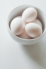 White eggs in a white bowl on a white background. 