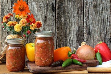 homemade salsa in glass jars with fresh vegetables on a rustic wood background