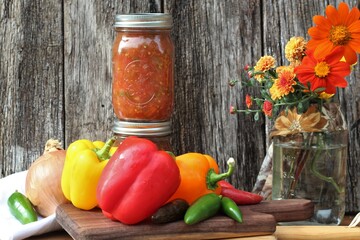 homemade salsa in glass jars with fresh vegetables on a rustic wood background