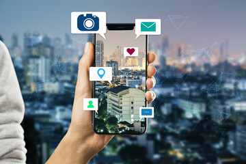 Close up of hand holding smartphone device with abstract polygonal mesh, camera, location pin, email and chat icons on night city background. 