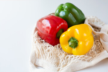Three multi-colored fresh bell peppers lie in a mesh bag on the kitchen table. Healthy food theme....