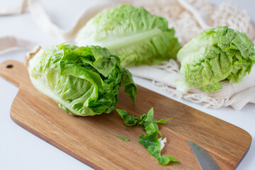 A green salad lies on a cutting wooden board next to a knife against the background of two other salads on the kitchen table. Healthy food theme.