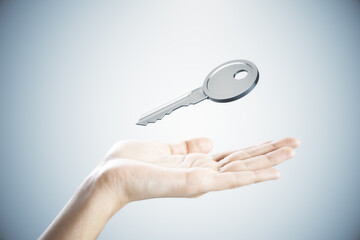 Close up of female hand holding silver key on gray background. Mortgage and purchase concept.