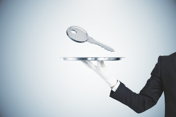 Close up of businessman hand holding silver tray with key on gray background. Mortgage and purchase concept.