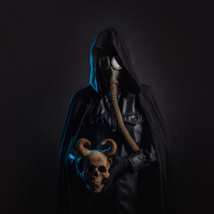 A post-apocalyptic concept. A cultist in a black hood and a gas mask on his face holds a human...