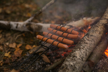 Sausages are fried on a grill by the fire.