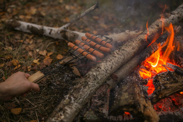 Sausages are fried on a grill by the fire.