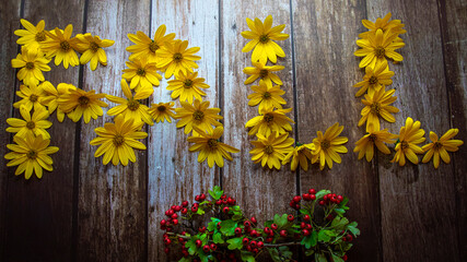 Autumn concept, word "autumn" laid out with yellow flowers on wooden background decorated with berries