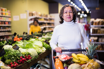 Portrait of positive interested elderly woman visiting supermarket food department for shopping