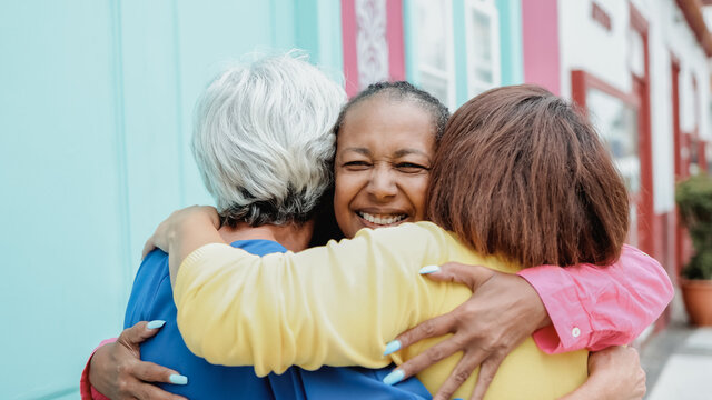 Multiracial senior women having fun together hugging outdoor in the city - Focus on african female face