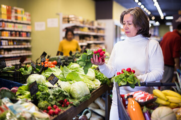 Elderly woman picks ripe radishes on grocery store shelves