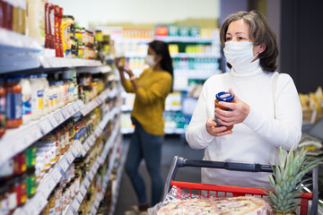 Elderly woman in protective face mask shopping in grocery store during pandemic. Concept of new life reality and precautions..
