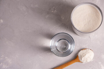 Collagen powder with a glass of water on a gray background with copy space.