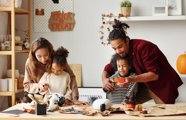 Young joyful african american family mother, father and two kids preparing for Halloween at home