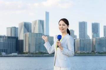 都市の前に立つ女性アナウンサー