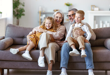 Happy family joyful little children hugging embracing with positive senior grandparents at home