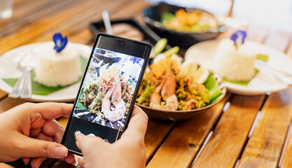 Fototapeta na wymiar Female hand uses the Mobile Phone take photo with the Thai food for recommending and share to social media.