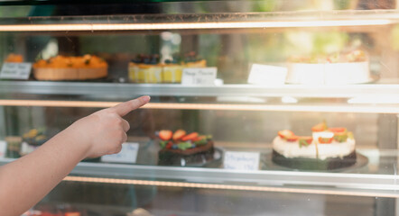 Female hand choosing hesitate between Vanilla cakes or Orange cake from the glasses showcase at the coffee shop.