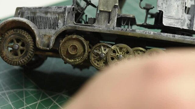 Scale Modeling. Mud Weathering and aging process on track wheels of military car. Man paints smudges of dirt on wheels on German 8ton Semi Track Plastic Scale Model.