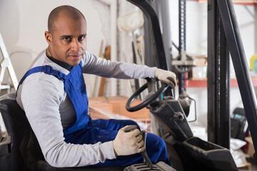 Fototapeta na wymiar Portrait of confident hispanic worker driving forklift in building materials store